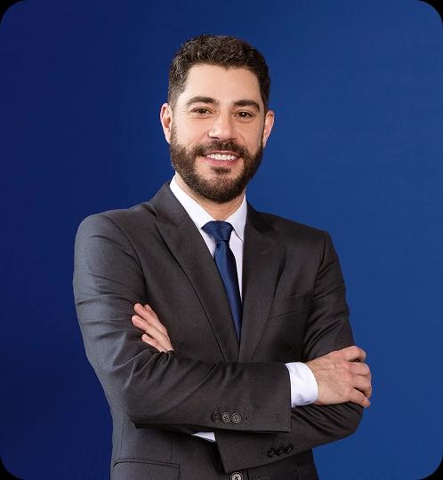 Evaristo Costa veste um terno e está de braços cruzados e sorrindo.