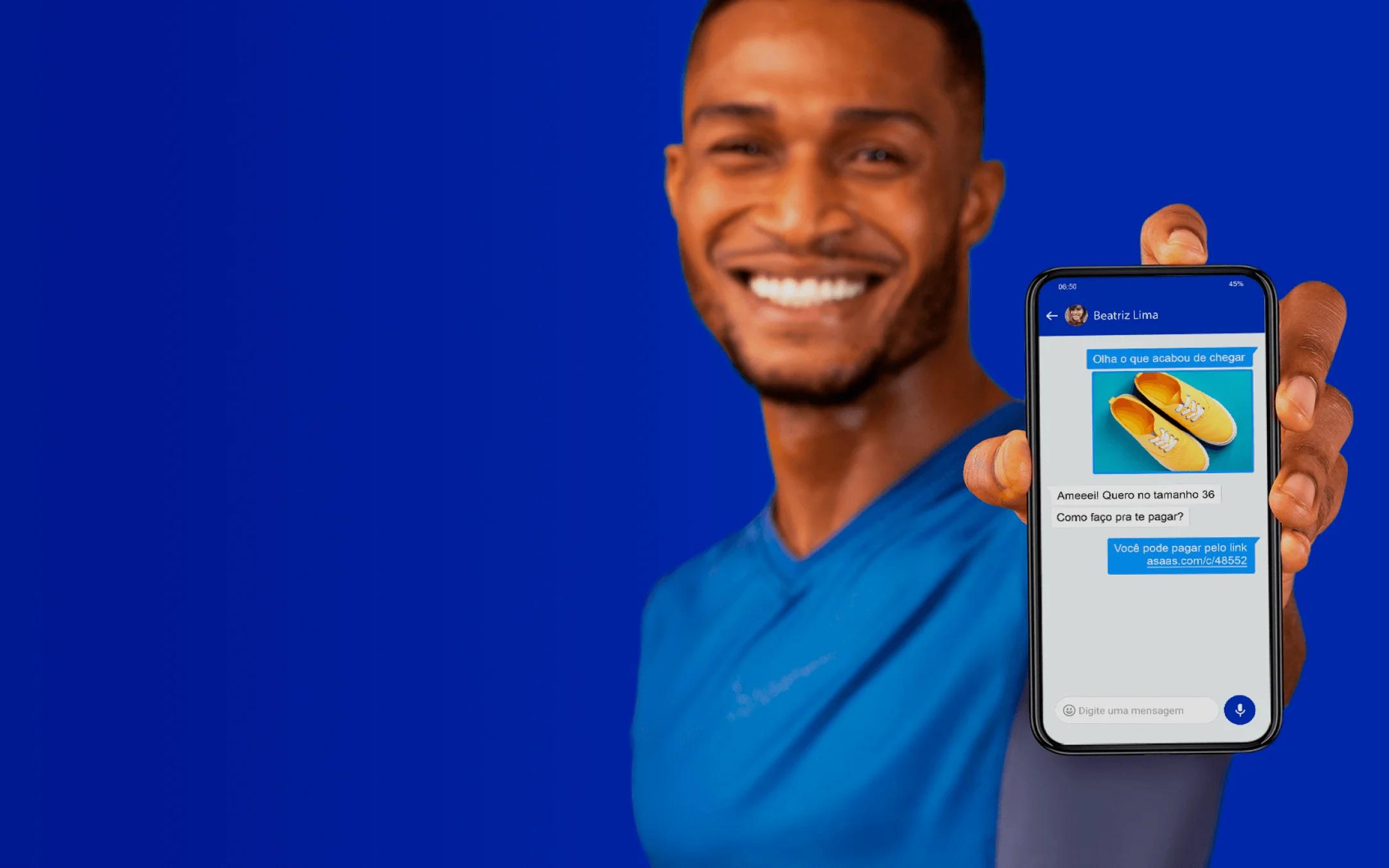 Homem sorri para a câmera enquanto segura um celular que mostra a tela de criação de link de pagamento.